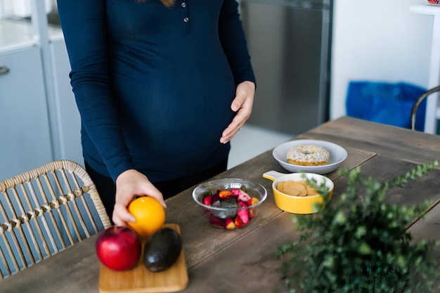 Photo cropped shot of pregnant woman touching her belly choosing from healthy salad chips and donut healthy and unhealthy food concept healthy and balanced diet during pregnancy
