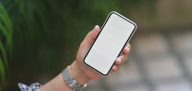 Cropped shot of professional businessman holding blank screen smartphone with blurred garden background