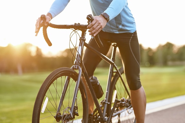 Cropped shot of professional road bicycle racer in sportswear cycling outdoors at sunset man