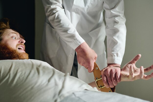 Cropped shot of psychiatrist binding hands of male patient with belts