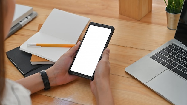 Cropped shot side view of young woman are using white blank screen smartphone on work desk at the office.