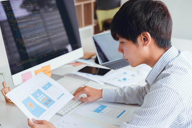 Cropped shot of startup UX UI front end designers developing programming and coding mobile application from prototype and wireframe layout. Mobile application developer workplace concept.