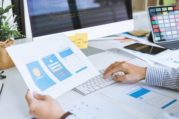 cropped shot of startup ux ui front end designers developing programming and coding mobile application from prototype and wireframe layout. mobile application developer workplace concept.
