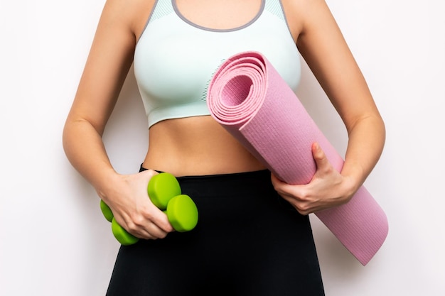 Cropped shot of a toned tanned slender young woman holding dumbbells and yoga mat Fitness workout