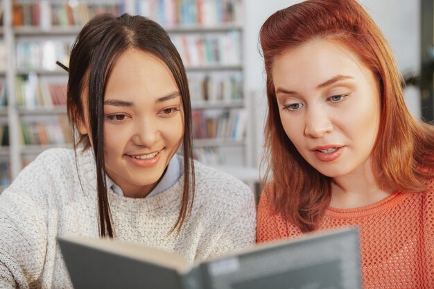 Cropped shot of two young female friends reading a book together at college library