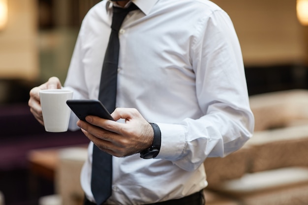 Cropped shot of unrecognizable businessman holding smartphone and coffee cup, copy space