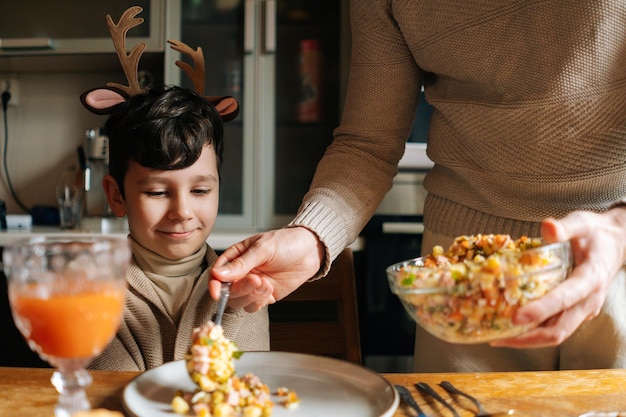 Cropped shot of unrecognizable young male father putting salad on plate to smiling child son