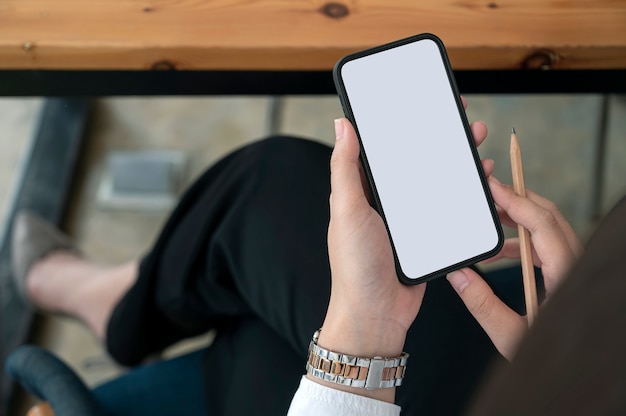 Cropped shot of woman hand holding blank screen smartphone while sitting at the table in office.