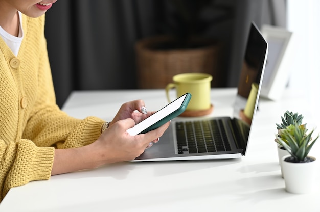 Cropped shot of a woman is using smartphone for typing messages, sharing social media at her workspace.