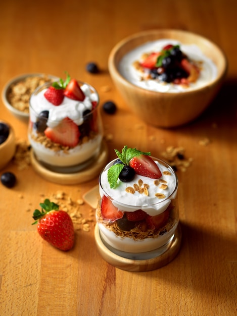 Cropped shot of wooden table with bowl and glasses of granola with Greek yogurt and fresh berries