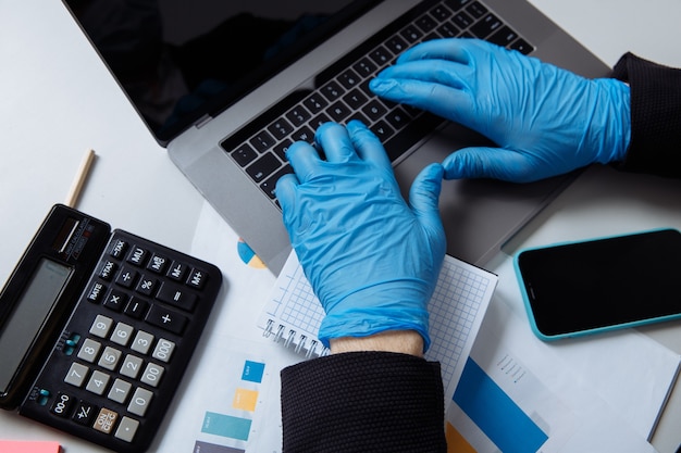 Обрезанный снимок работника в защитных перчатках во время работы с ноутбуком в офисе.