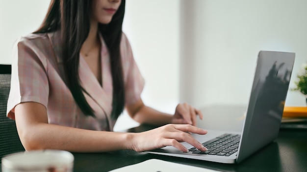 Cropped shot of working woman typing business email searching\
information on laptop computer