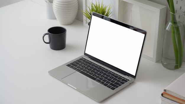 Cropped shot of  workspace with blank screen laptop, office supplies, decorations and coffee cup on white desk