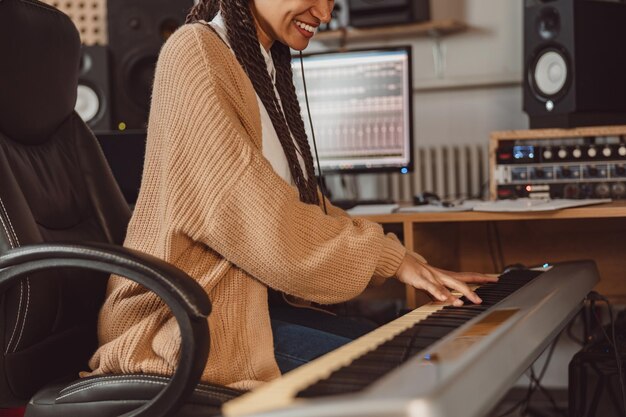 Cropped shot of young African female musician playing electronic piano synthesizer in the modern recording music studio