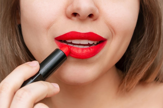 Cropped shot of young beautiful caucasian blonde woman applying\
a bright red color lipstick on lips