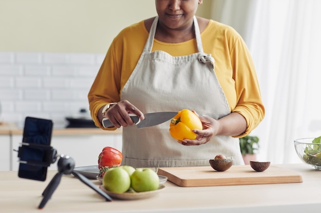 Cropped shot of young black woman cooking healthy meal in kitchen and recording video with smartphon