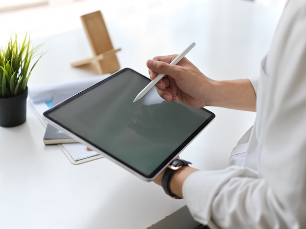 Обрезанный снимок молодого бизнесмена, пишущего на макете планшета в современном офисе