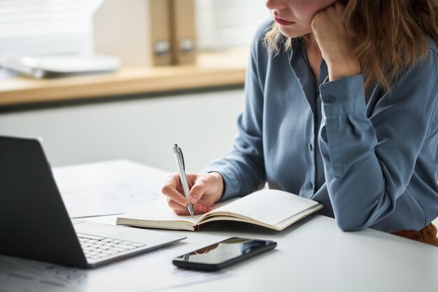 Cropped shot of young businesswoman or student in blue shirt holding pen