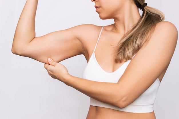 Photo cropped shot of a young caucasian blonde woman grabbing skin on her upper arm with excess fat