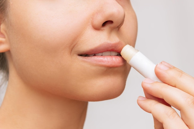 Cropped shot of a young caucasian smiling woman applying a hygienic lipstick on her lips