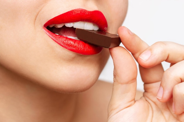 Cropped shot of a young caucasian woman with glossy red color lips eating and enjoying a chocolate