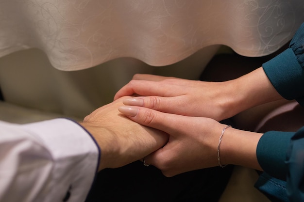 Cropped shot of young couple holding hands while sitting together. Focus on hands.