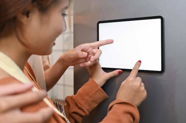 cropped shot of young couple interacting with digital tablet mounted on the door of a refrigerator