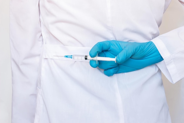 Cropped shot of young female doctor in a white coat holding a syringe with a needle behind her back