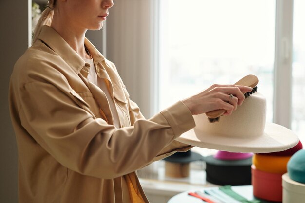 Cropped shot of young female entrepreneur cleaning hat with brush