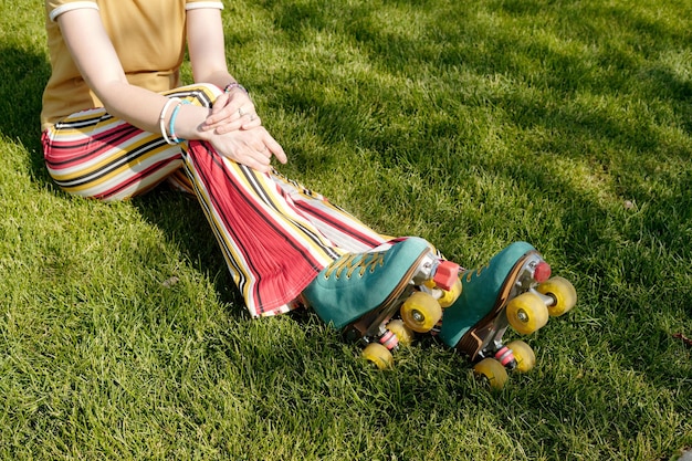 草の上に座っている縞模様のパンツを履いた若い女性ローラー スケート選手のショットをトリミング