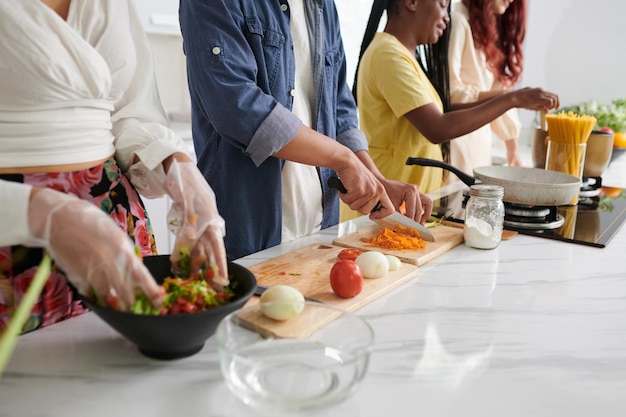 Cropped shot of young intercultural friends in casualwear cooking food