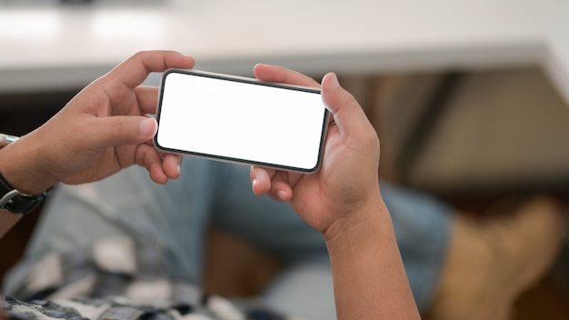 Cropped shot of young male using his blank screen smartphone  with relax sitting position