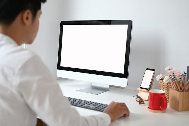 Обрезанный снимок молодого человека, планирующего свой проект на компьютере с белым экраном на белом столе.