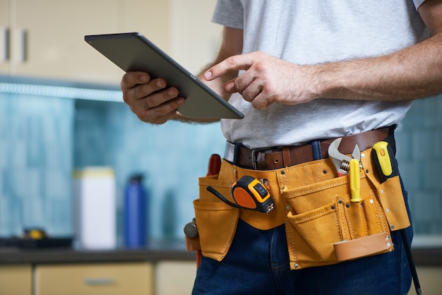 Cropped shot of young repairman wearing a tool belt with various tools using digital tablet while