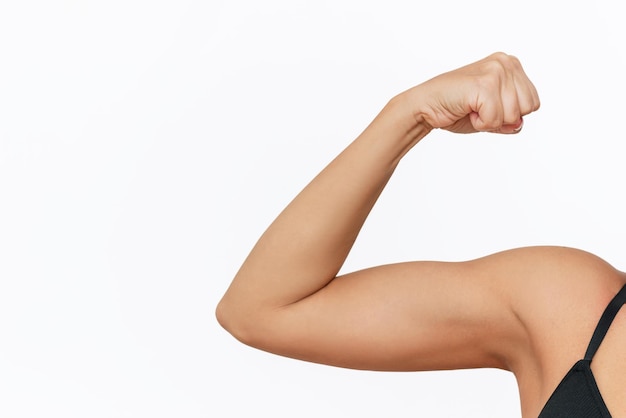 Cropped shot of young tanned strong fit woman raising arm and showing bicep on a white background