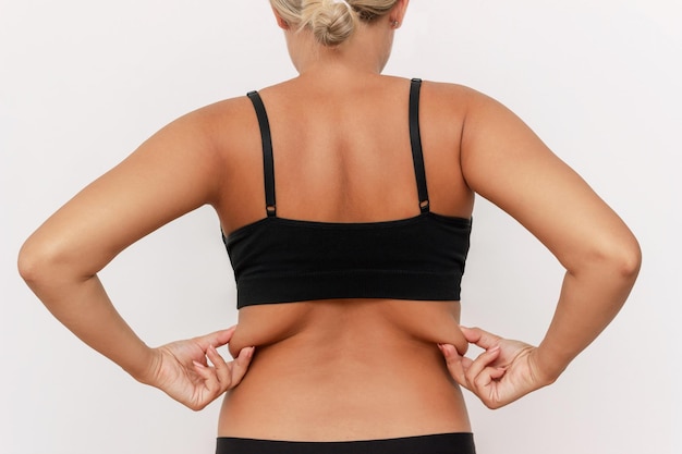 Cropped shot of a young tanned woman in black underwear holding fat folds on her back. Sagging skin