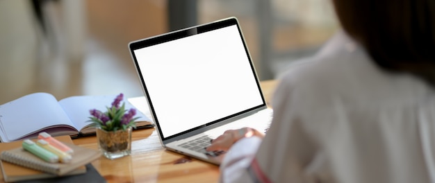 Cropped shot of  young university student typing on blank screen laptop with notebook and stationery