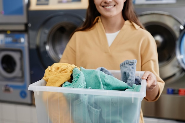 cropped shot of young woman holding container with heap of clean clothes