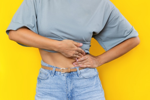 Cropped shot of a young woman holding her side with her hands isolated on color yellow background