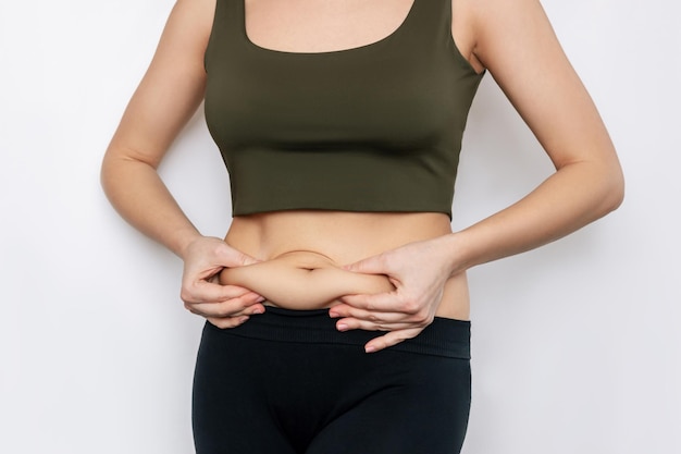 A cropped shot of a young woman holding herself by a fat on her stomach Hormonal belly