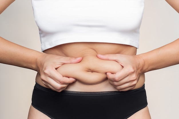 Foto un'inquadratura ritagliata di una giovane donna che si tiene per il grasso sullo stomaco che mangia troppo peso in eccesso
