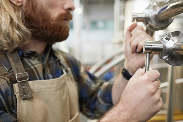 Cropped side view of bearded brewmaster operating machines at beer making factory, copy space