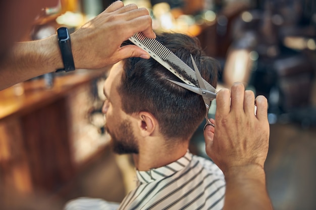 Cropped side-view photo of a brunette man getting a fresh new hair-style at a barbershop