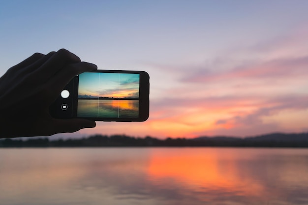 写真 夕暮れの間雲の空に照らされた湖を写真に撮るカットされたシルエットの手