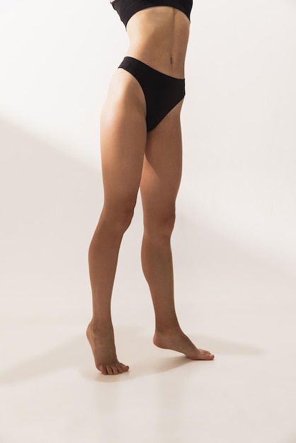 흰색 스튜디오 위에 검은색 속옷을 입은 날씬한 몸매를 갖춘 여성 신체의 자른 스튜디오 이미지