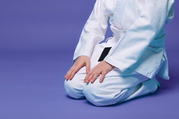 Cropped view of an aikido fighter in a white kimono during the practice of oriental martial arts isolated over purple background with copy ad space