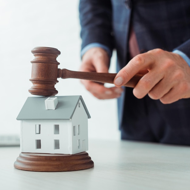 Cropped view of auctioneer hitting model of house with gavel