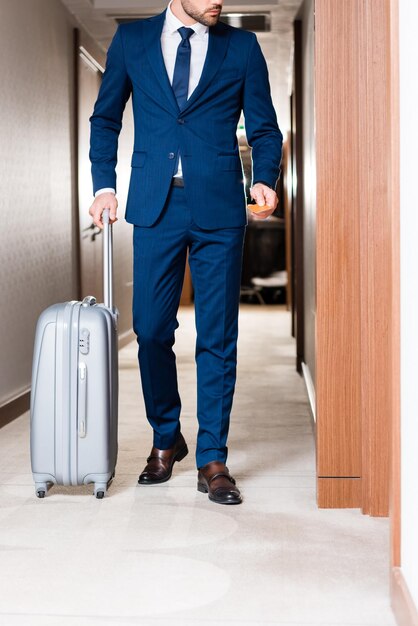 Cropped view of bearded businessman holding hotel card while standing with suitcase