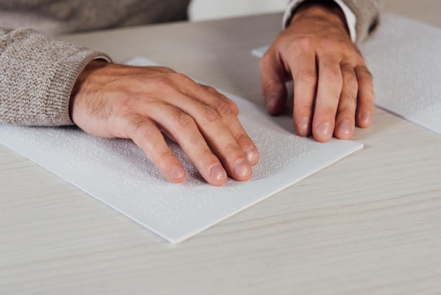 Обрезанный вид связанного человека, читающего шрифт Брайля на бумаге за столом
