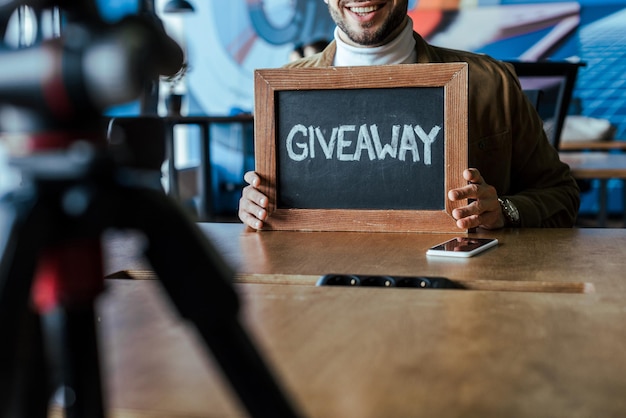 Photo cropped view of blogger showing board with giveaway lettering and smiling at table in coworking